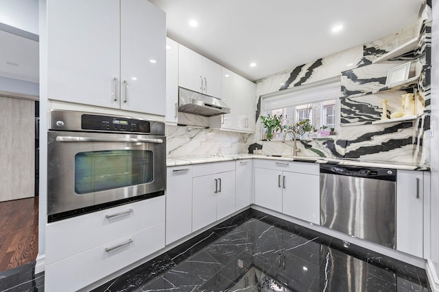 kitchen featuring tasteful backsplash, stainless steel appliances, under cabinet range hood, white cabinetry, and a sink