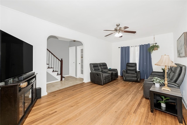 living room with arched walkways, stairway, wood finished floors, and a ceiling fan