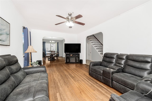 living area featuring stairs, arched walkways, ceiling fan with notable chandelier, and wood finished floors