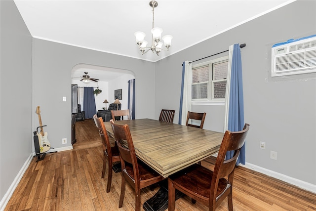 dining room featuring arched walkways, light wood-style floors, baseboards, and crown molding