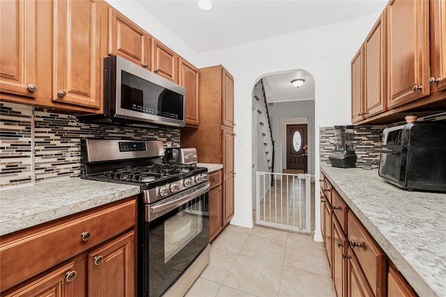 kitchen with arched walkways, light tile patterned floors, appliances with stainless steel finishes, brown cabinets, and tasteful backsplash