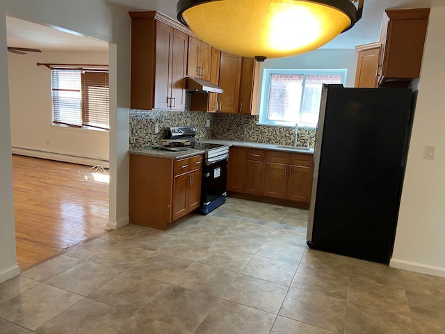 kitchen with appliances with stainless steel finishes, brown cabinetry, a baseboard heating unit, a sink, and under cabinet range hood