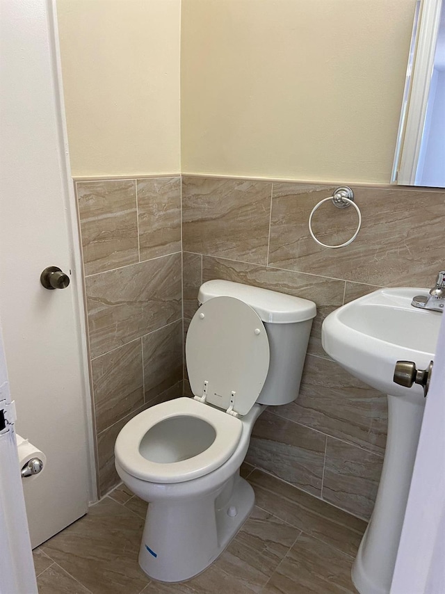 half bath featuring wainscoting, tile walls, and toilet