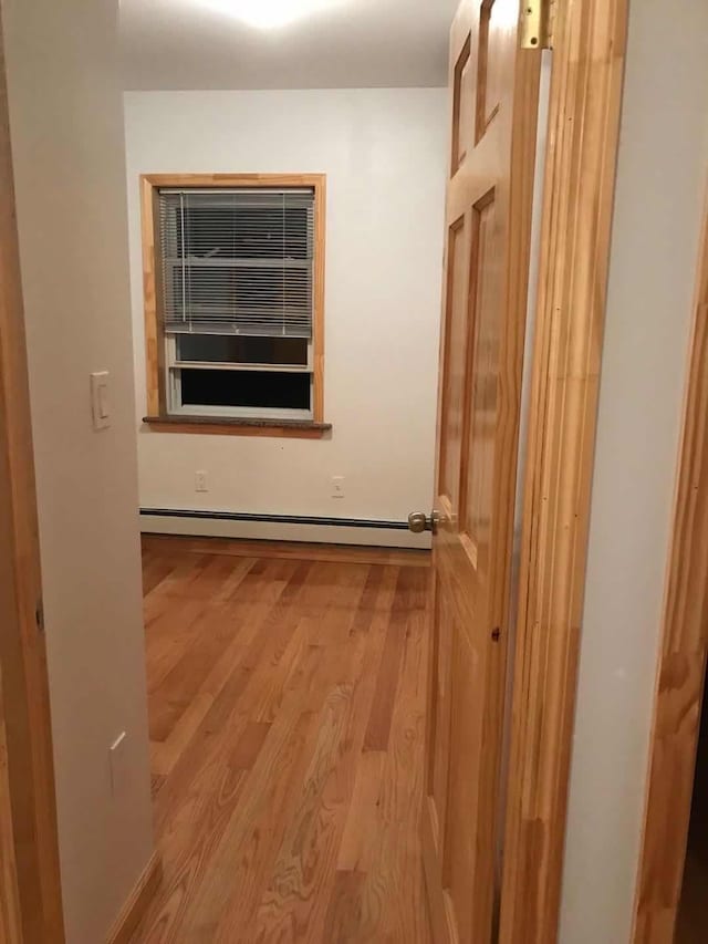 corridor with a baseboard heating unit and light wood-style floors