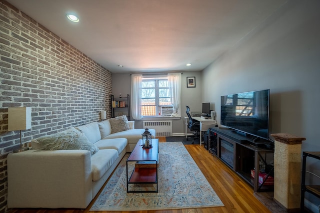 living area with radiator, brick wall, an accent wall, wood finished floors, and recessed lighting