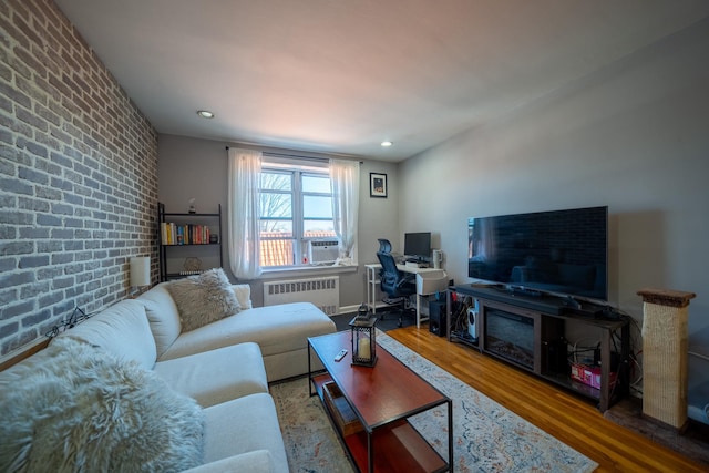 living area featuring brick wall, radiator heating unit, an accent wall, wood finished floors, and recessed lighting