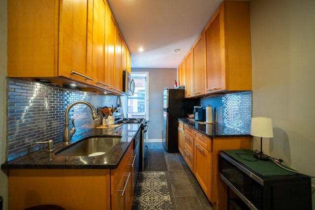 kitchen with brown cabinetry, decorative backsplash, appliances with stainless steel finishes, dark stone countertops, and a sink
