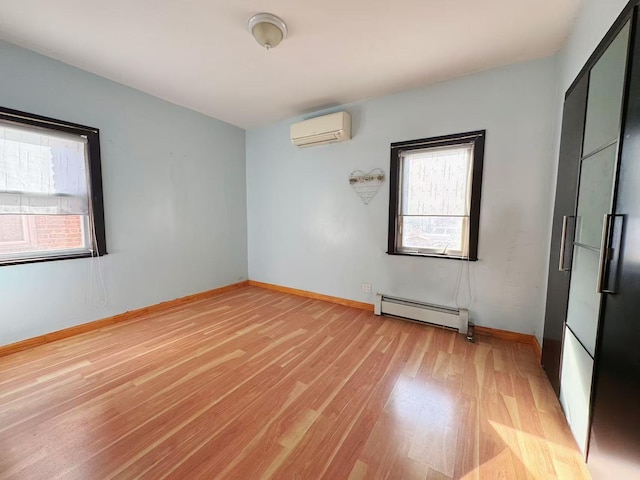 spare room with a baseboard heating unit, a wall unit AC, light wood-style flooring, and baseboards