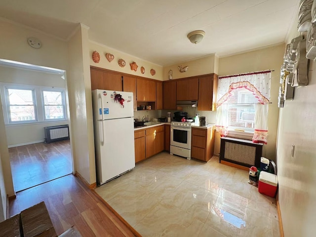 kitchen featuring light countertops, radiator heating unit, brown cabinetry, white appliances, and under cabinet range hood