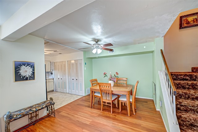 dining room featuring visible vents, light wood-style floors, ceiling fan, baseboards, and stairs