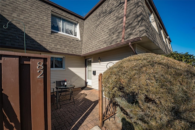 view of property exterior with a shingled roof, mansard roof, and a patio