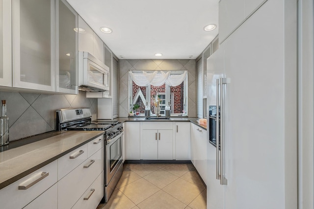 kitchen with white microwave, decorative backsplash, stainless steel gas range, and light tile patterned flooring