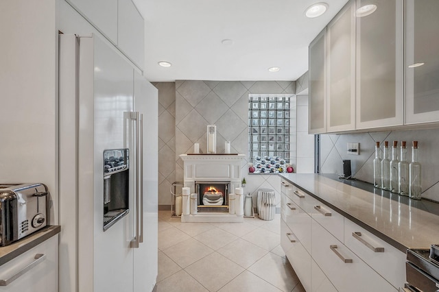 kitchen featuring dark stone counters, light tile patterned flooring, glass insert cabinets, tile walls, and refrigerator with ice dispenser