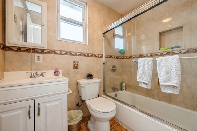 bathroom featuring toilet, combined bath / shower with glass door, tile walls, and vanity