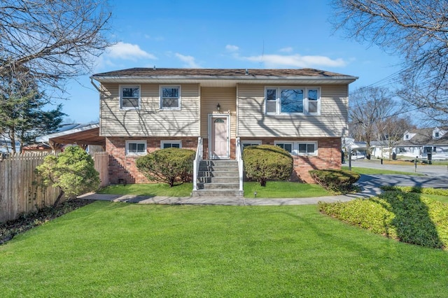 split foyer home featuring brick siding, fence, and a front lawn