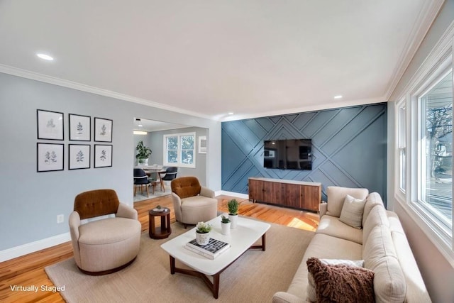 living area featuring an accent wall, plenty of natural light, crown molding, and wood finished floors