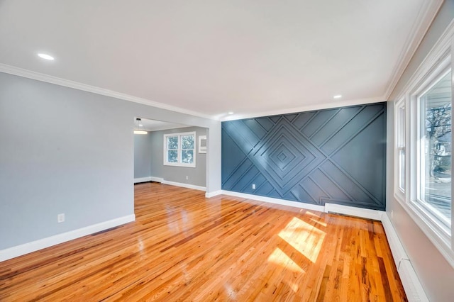 unfurnished room with light wood-style flooring, an accent wall, baseboards, and crown molding