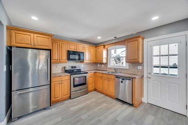 kitchen with appliances with stainless steel finishes, a sink, light wood-style flooring, and tasteful backsplash