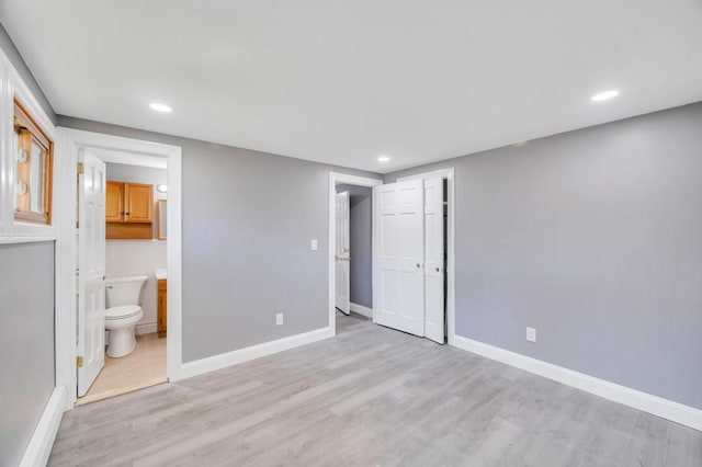 unfurnished bedroom featuring ensuite bath, light wood-style flooring, baseboards, and recessed lighting