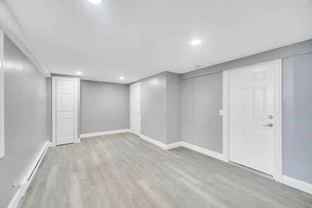 finished below grade area featuring light wood finished floors, baseboard heating, recessed lighting, and baseboards