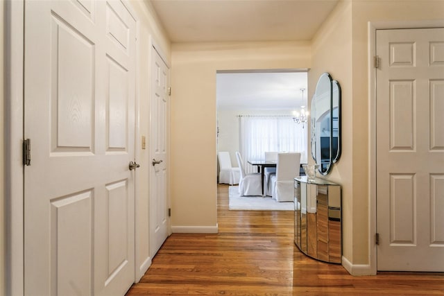 corridor featuring baseboards, an inviting chandelier, and wood finished floors