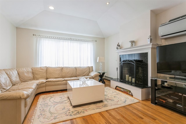 living area featuring a fireplace with raised hearth, wood finished floors, vaulted ceiling, baseboard heating, and a wall mounted air conditioner