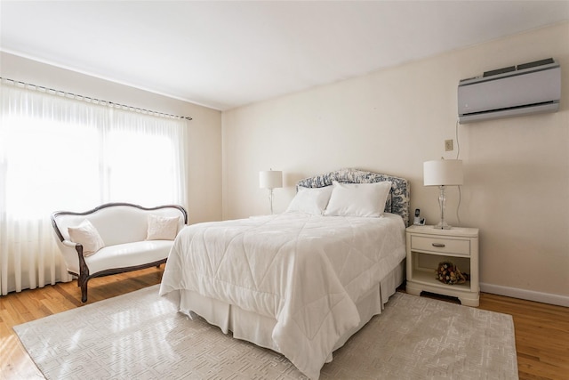 bedroom featuring a wall unit AC, wood finished floors, and baseboards