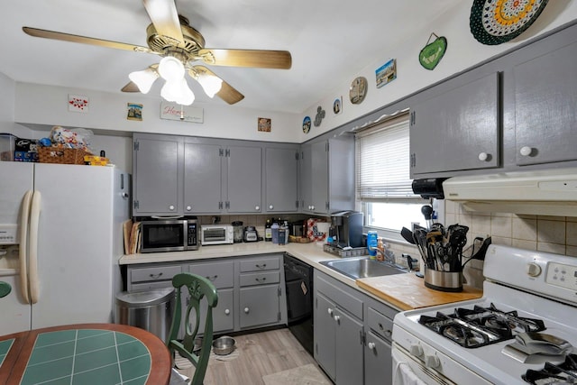 kitchen with gray cabinetry, under cabinet range hood, white appliances, a sink, and backsplash