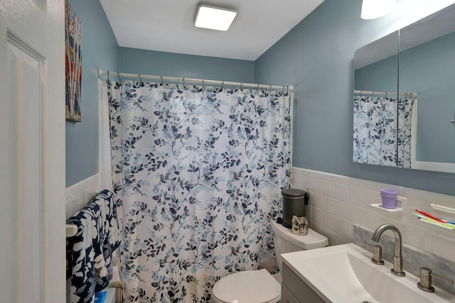 bathroom featuring toilet, a wainscoted wall, tile walls, and a shower with curtain