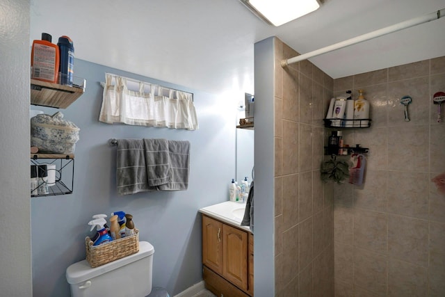 bathroom featuring toilet, tiled shower, and vanity