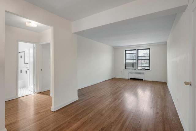 empty room with cooling unit, radiator, baseboards, and wood finished floors