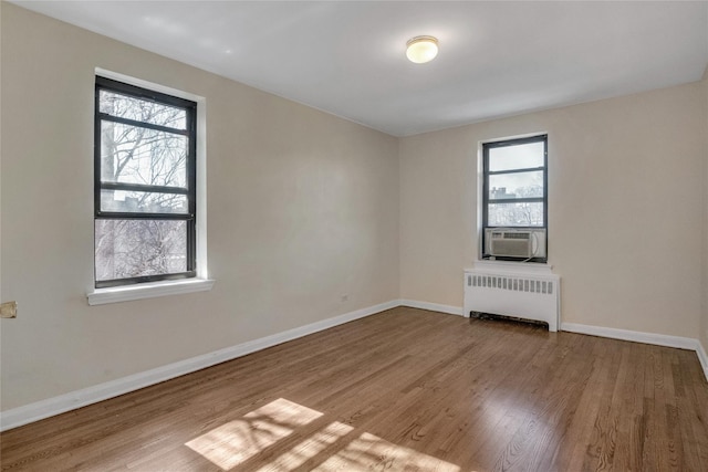 empty room with radiator heating unit, wood finished floors, a wealth of natural light, and baseboards