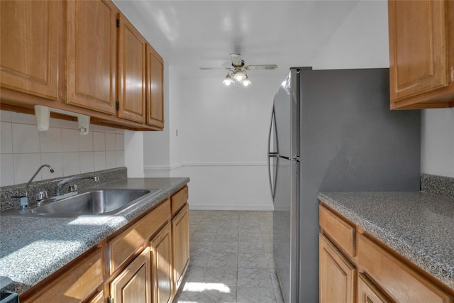 kitchen with brown cabinetry, a ceiling fan, freestanding refrigerator, a sink, and backsplash