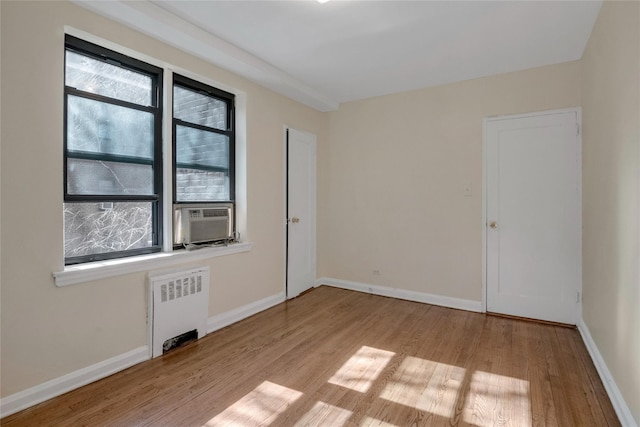 unfurnished room featuring cooling unit, baseboards, radiator heating unit, and wood finished floors