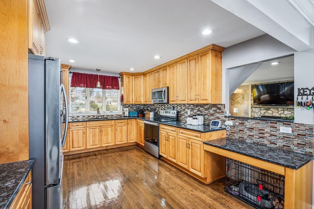 kitchen with decorative backsplash, dark stone counters, appliances with stainless steel finishes, dark wood-type flooring, and a sink