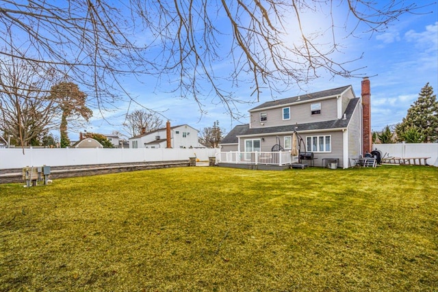 rear view of property with a fenced backyard, a chimney, a wooden deck, and a yard