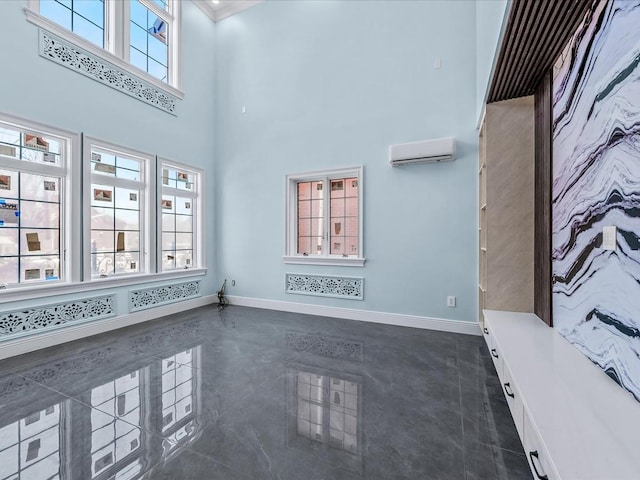 unfurnished room with a wall mounted air conditioner, a towering ceiling, and baseboards