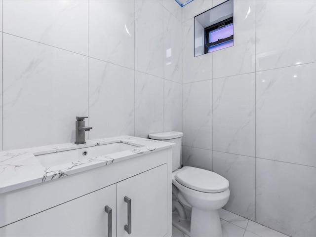 bathroom with toilet, marble finish floor, tile walls, and vanity