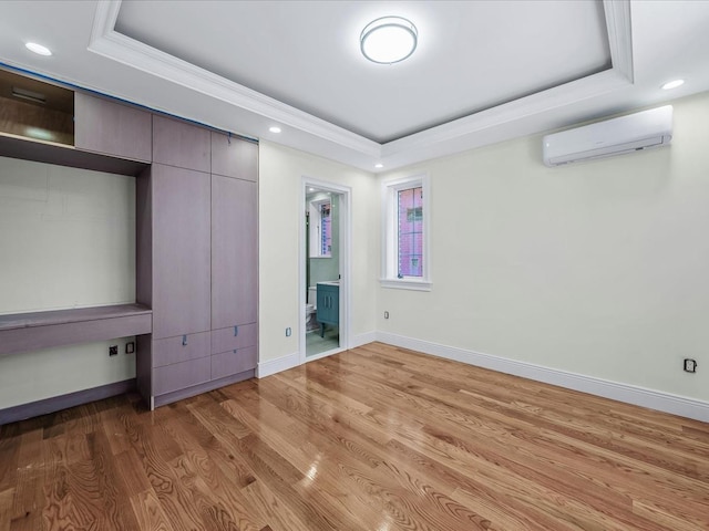 unfurnished bedroom with a wall unit AC, recessed lighting, a raised ceiling, light wood-style floors, and baseboards