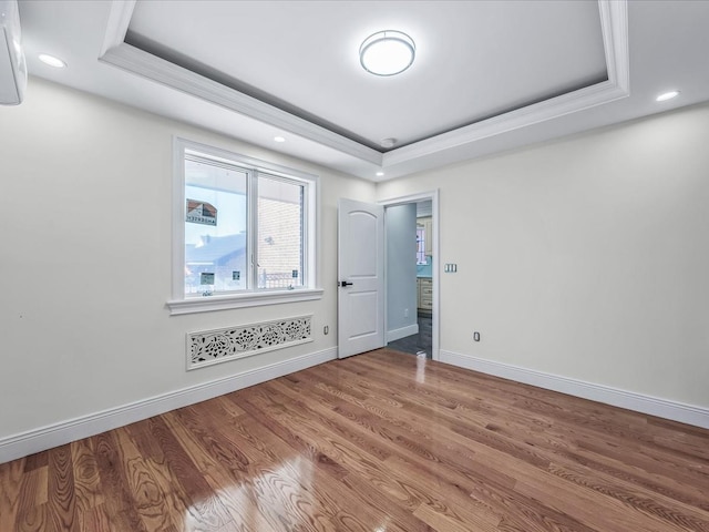 empty room with a tray ceiling, recessed lighting, baseboards, and wood finished floors