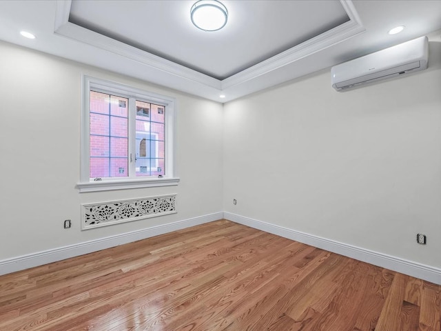 spare room featuring baseboards, a raised ceiling, wood finished floors, crown molding, and an AC wall unit