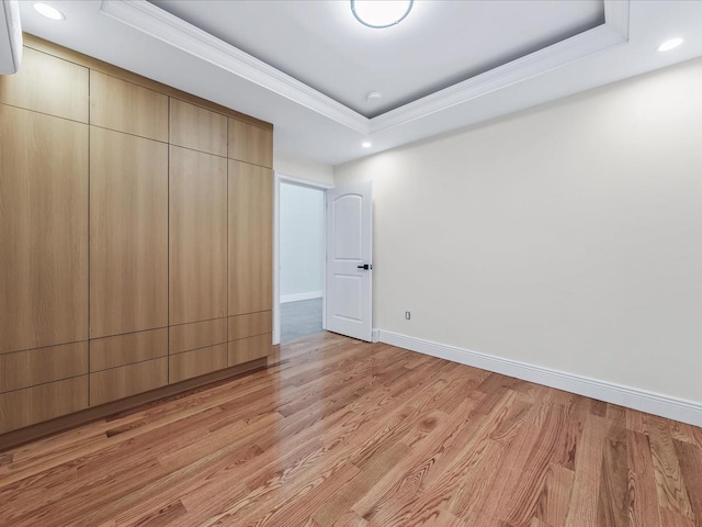 unfurnished bedroom with light wood finished floors, baseboards, a tray ceiling, crown molding, and recessed lighting