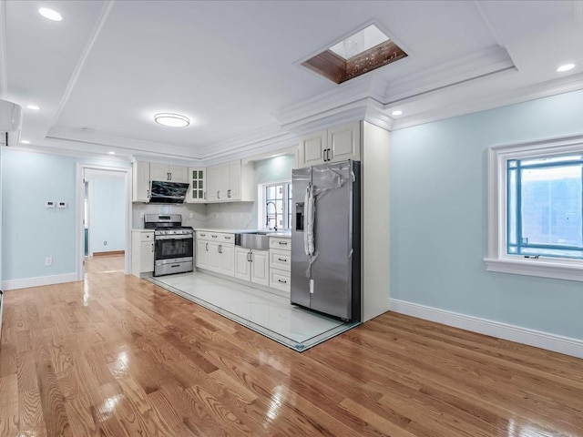 kitchen with light wood-type flooring, appliances with stainless steel finishes, a raised ceiling, and ornamental molding