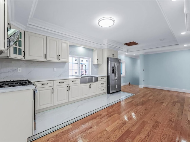 kitchen with a tray ceiling, stainless steel appliances, light countertops, ornamental molding, and a sink