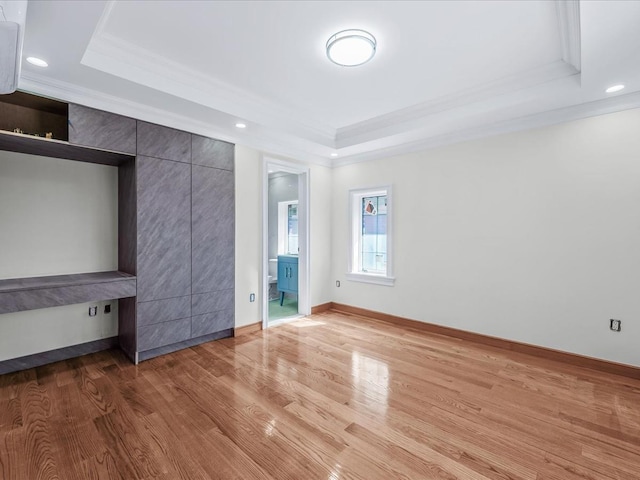 unfurnished bedroom with ornamental molding, wood finished floors, a raised ceiling, and recessed lighting