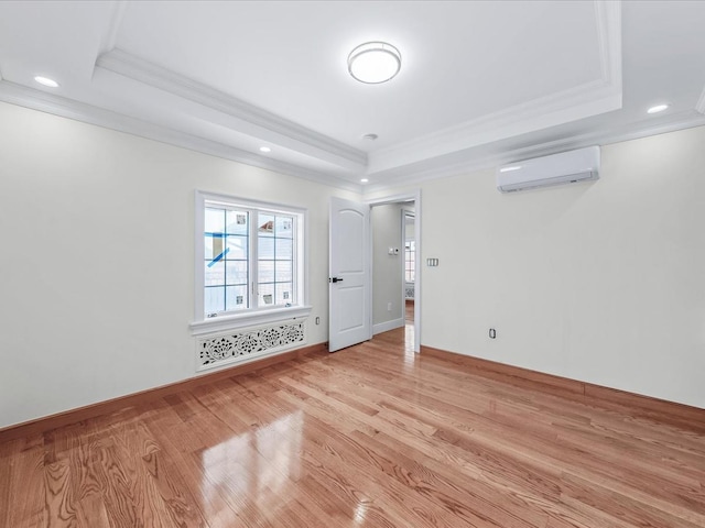 spare room featuring an AC wall unit, ornamental molding, a raised ceiling, and light wood-style flooring