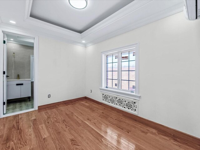 unfurnished bedroom with baseboards, wood finished floors, ensuite bathroom, a tray ceiling, and crown molding