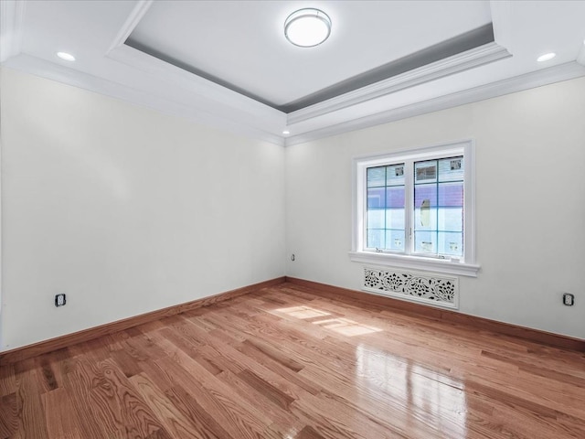 spare room with wood finished floors, baseboards, radiator heating unit, a raised ceiling, and crown molding