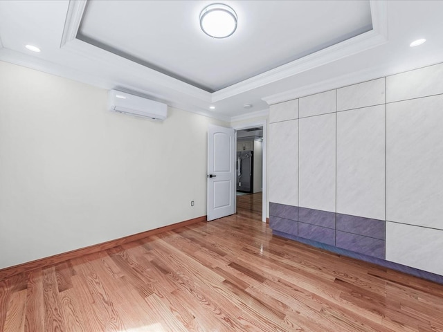 empty room featuring baseboards, ornamental molding, a wall mounted air conditioner, a tray ceiling, and light wood-style floors