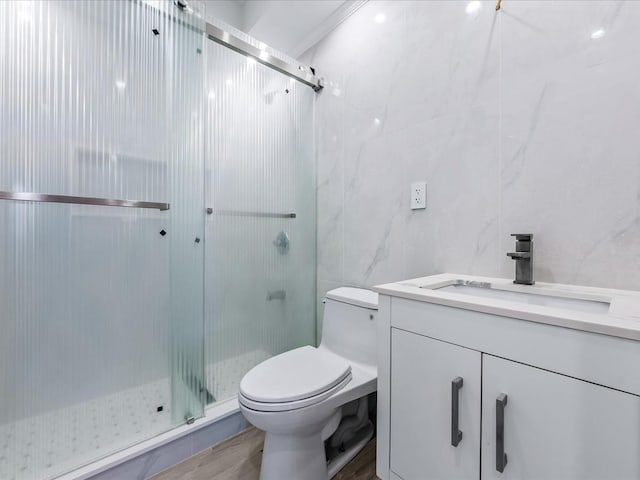 bathroom featuring toilet, wood finished floors, vanity, tile walls, and a stall shower